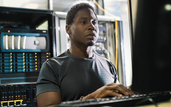 Young Black Man Working In A Server Room Administering The System