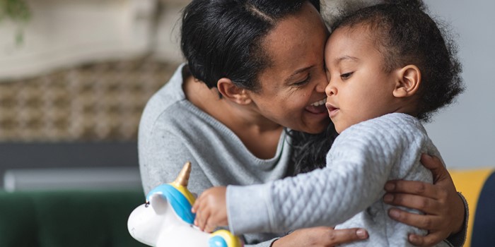 African American Mother Is Hugging Her Baby Son Proudly While He Is Putting Money Away In A Piggy Bank