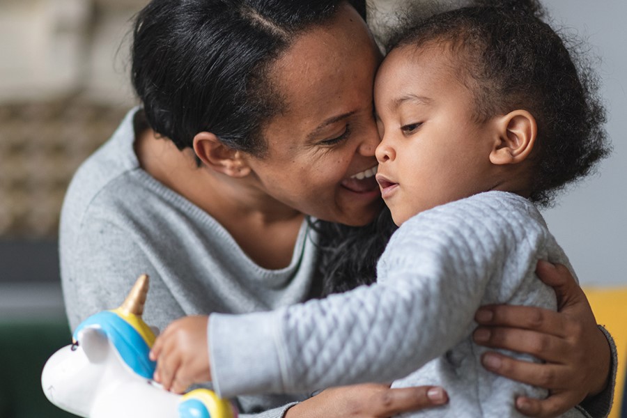 African American Mother Is Hugging Her Baby Son Proudly While He Is Putting Money Away In A Piggy Bank