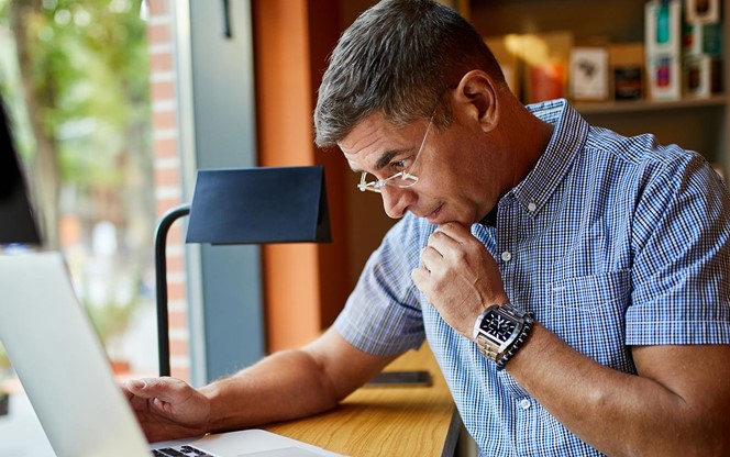 Mature Businessman Working On Laptop In Cafe