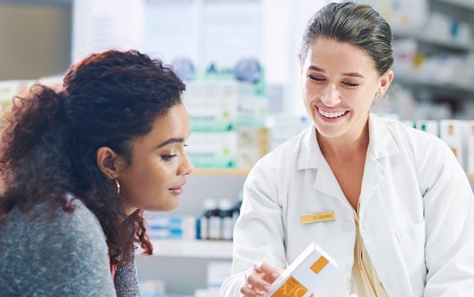 Young Pharmacist Using A Digital Tablet While Assisting A Customer In A Chemist