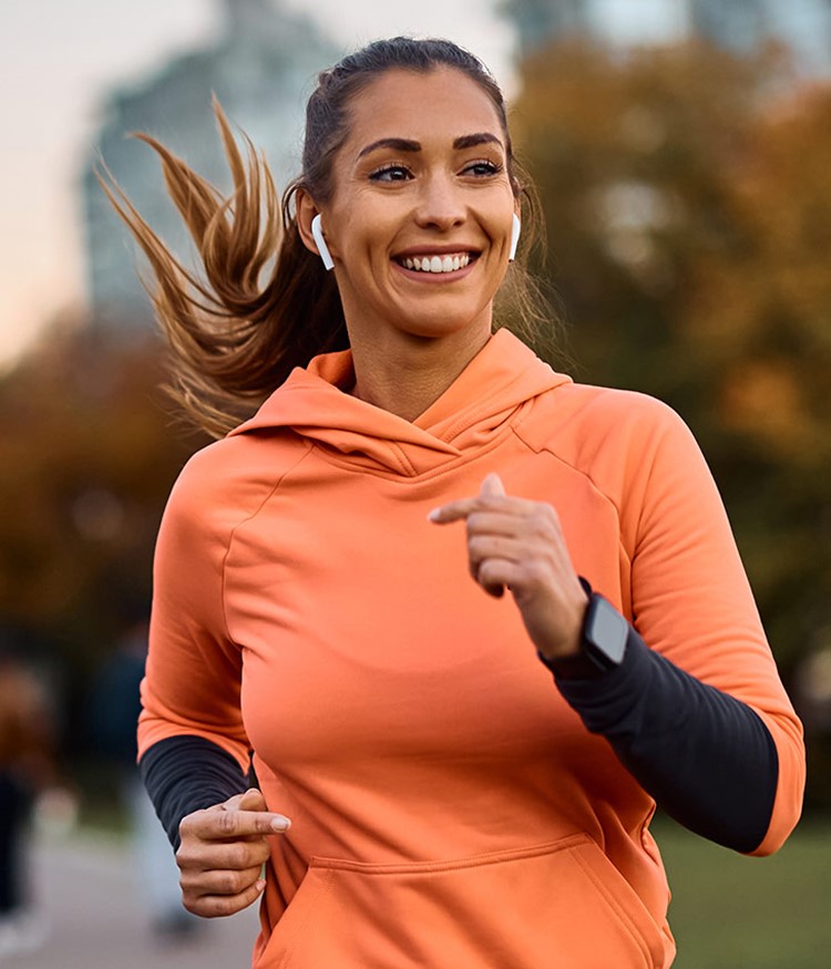 Happy Sportswoman With Earbuds Running In The Park