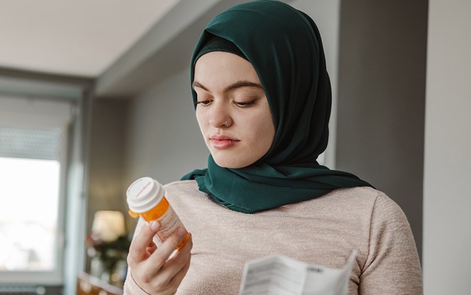 A Young Asian Woman Reading The Ingredients On A Bottle Of Pills