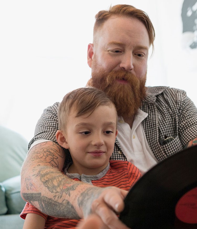 Father And Son Looking At Records On Living Room Floor