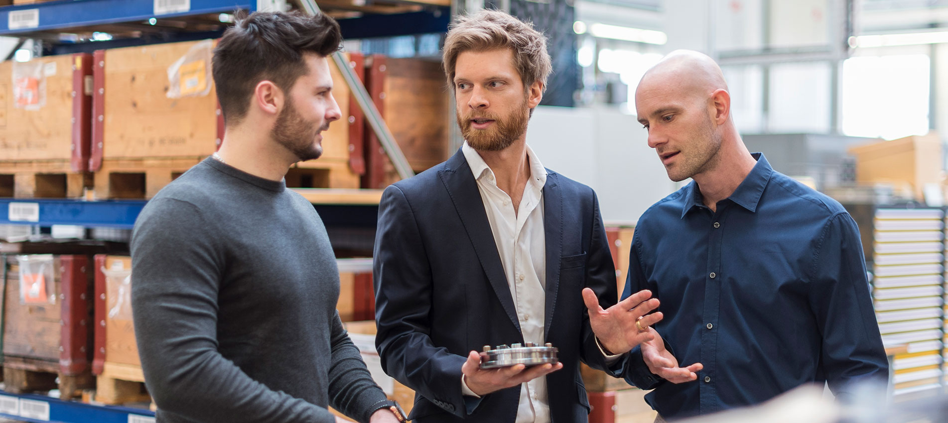 Three Men Talking In Factory Storeroom