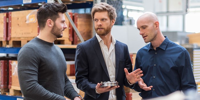 Three Men Talking In Factory Storeroom