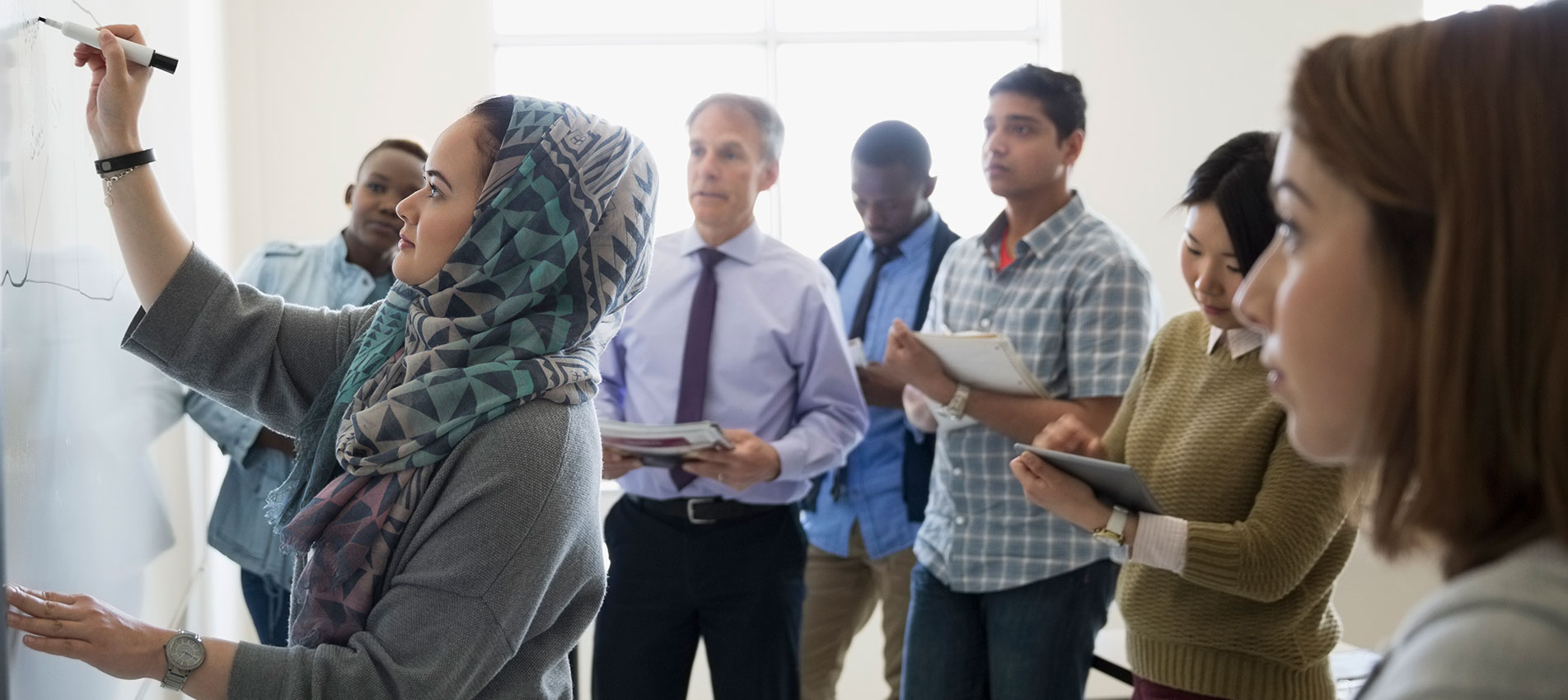Classmates Watching ESL Student In Hijab Writing On Whiteboard