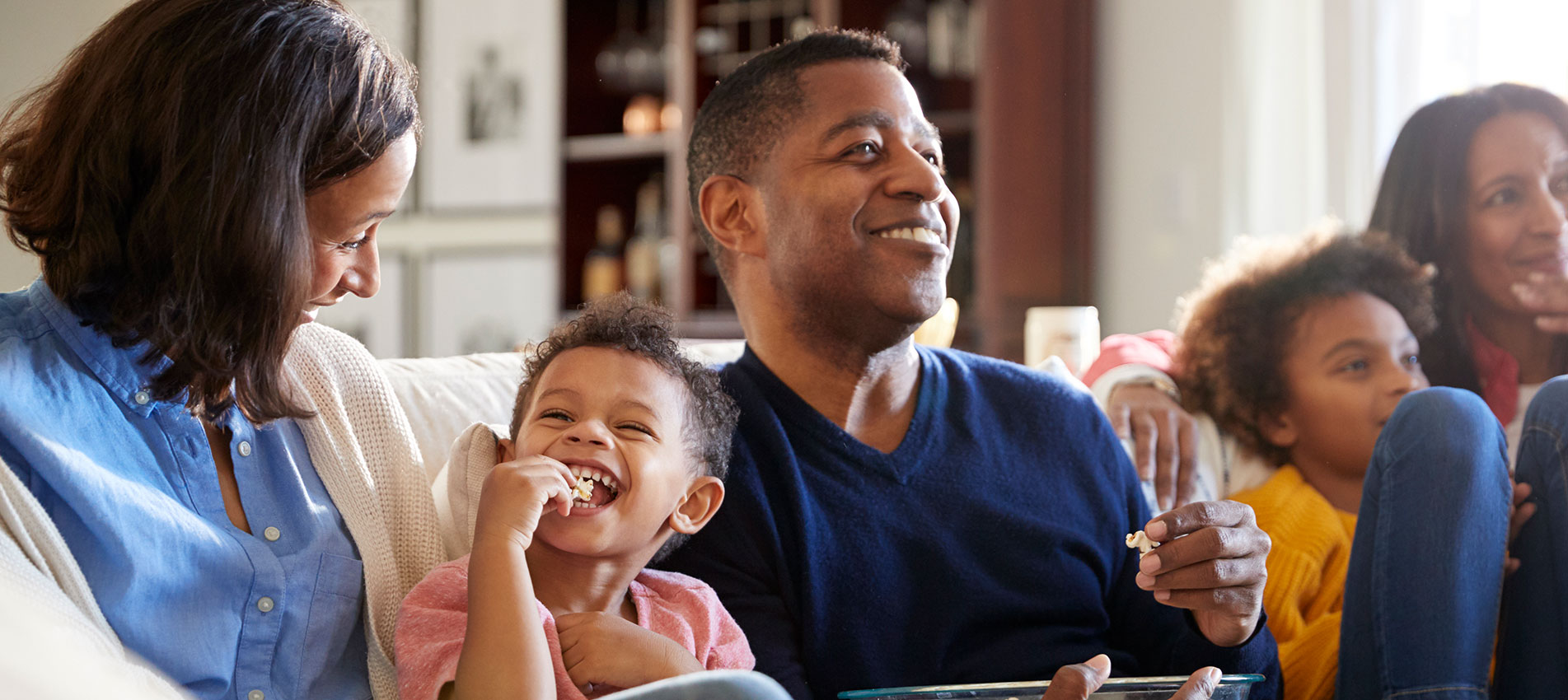 Family Sitting On The Sofa In Living Room Watching TV And Eating Popcorn