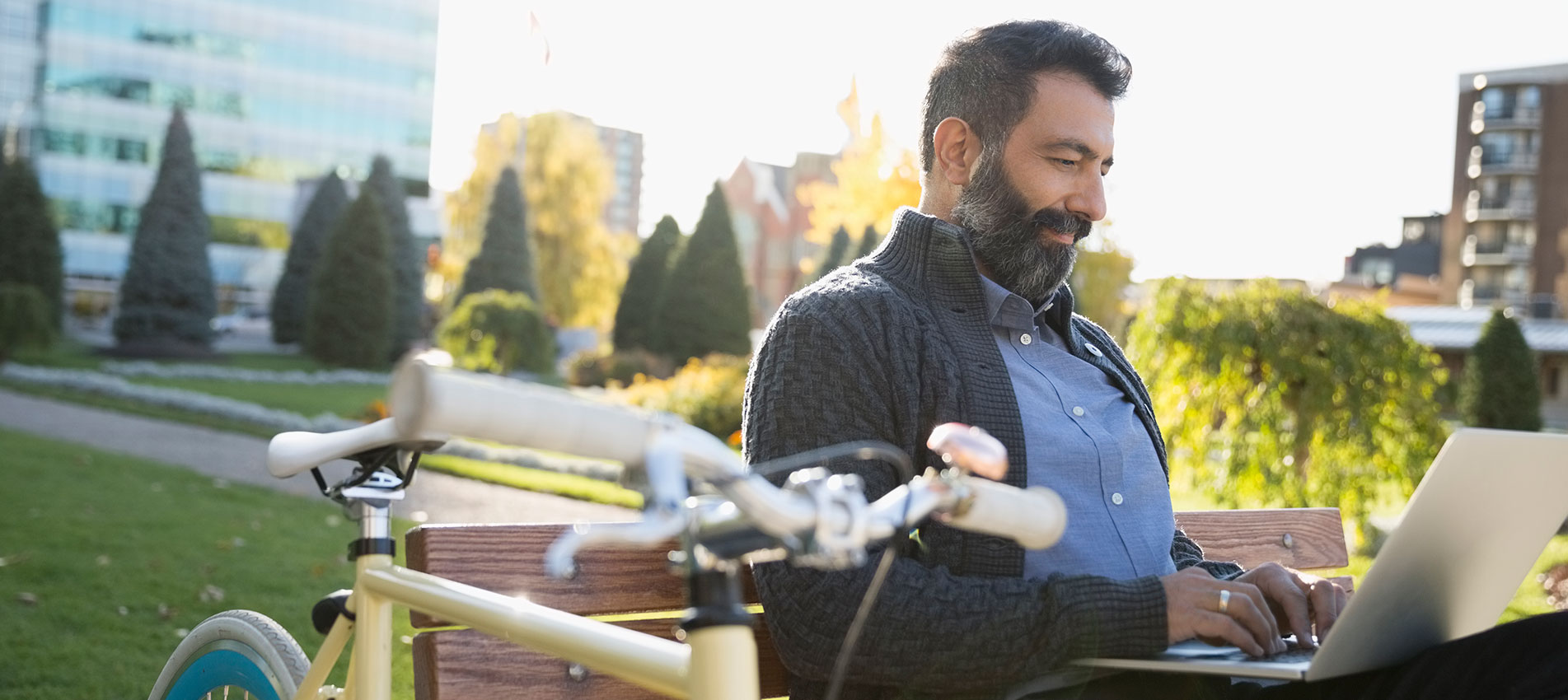 Commuter With Bicycle Using Laptop On Park Bench