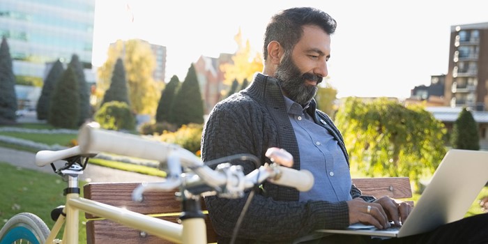 Commuter With Bicycle Using Laptop On Park Bench