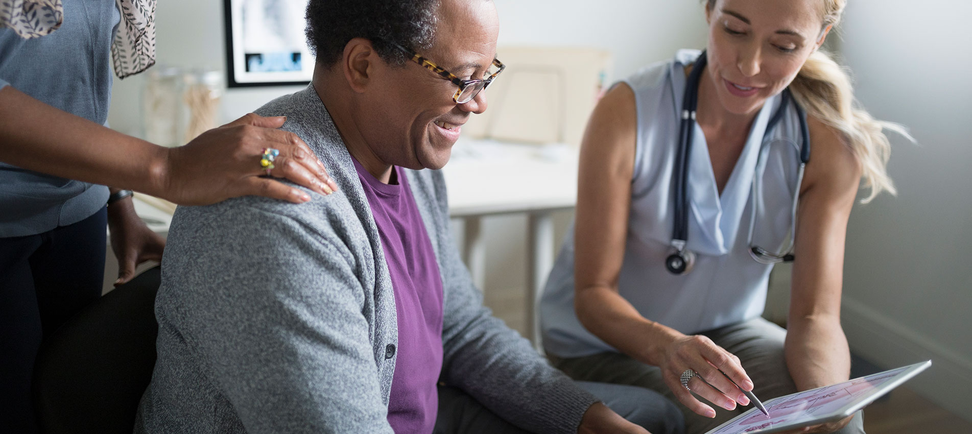 Doctor Showing Digital Tablet To Patient In Examination Room