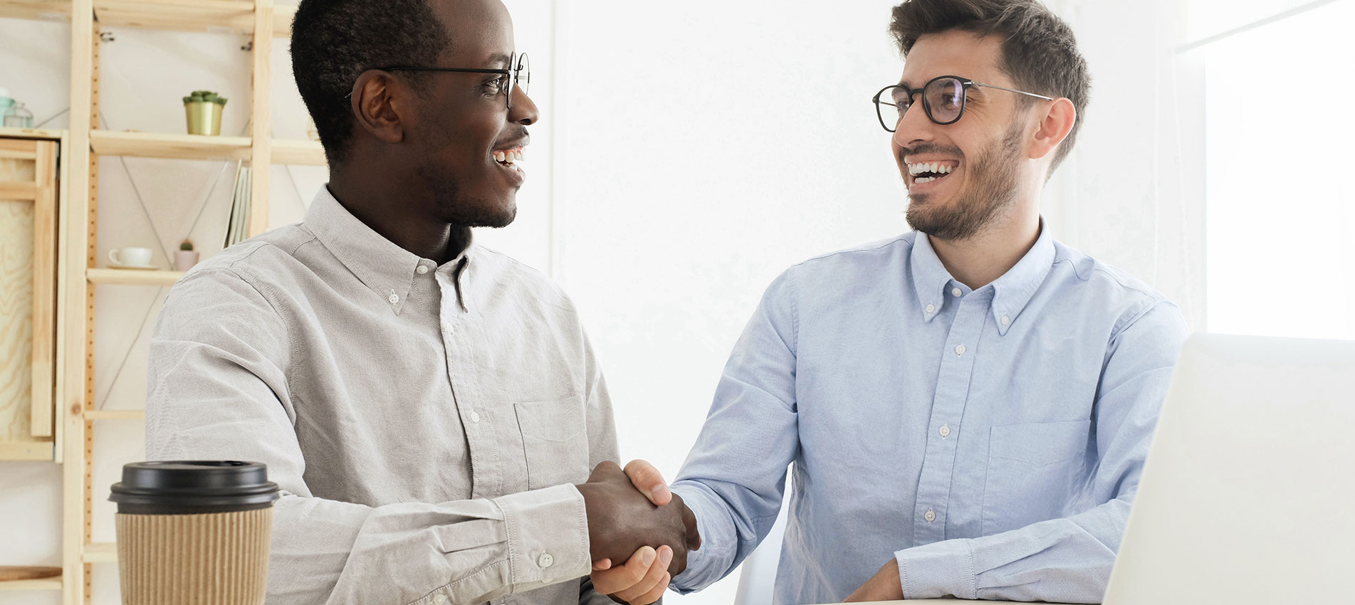 Young multiethnic men in smart casual wear shaking hands while working together
