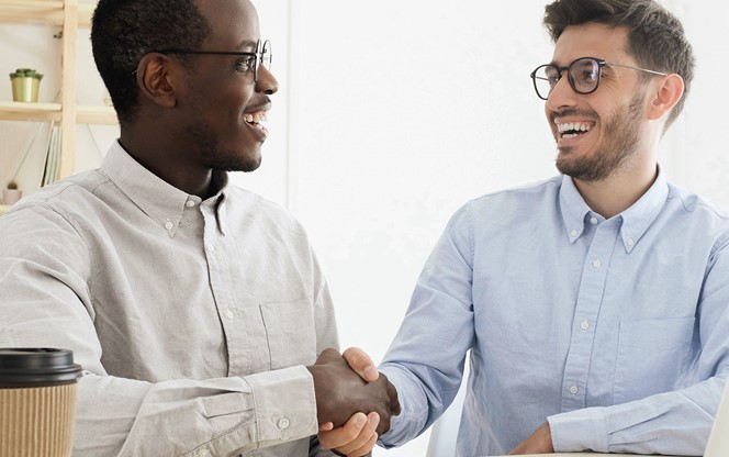 Young multiethnic men in smart casual wear shaking hands while working together