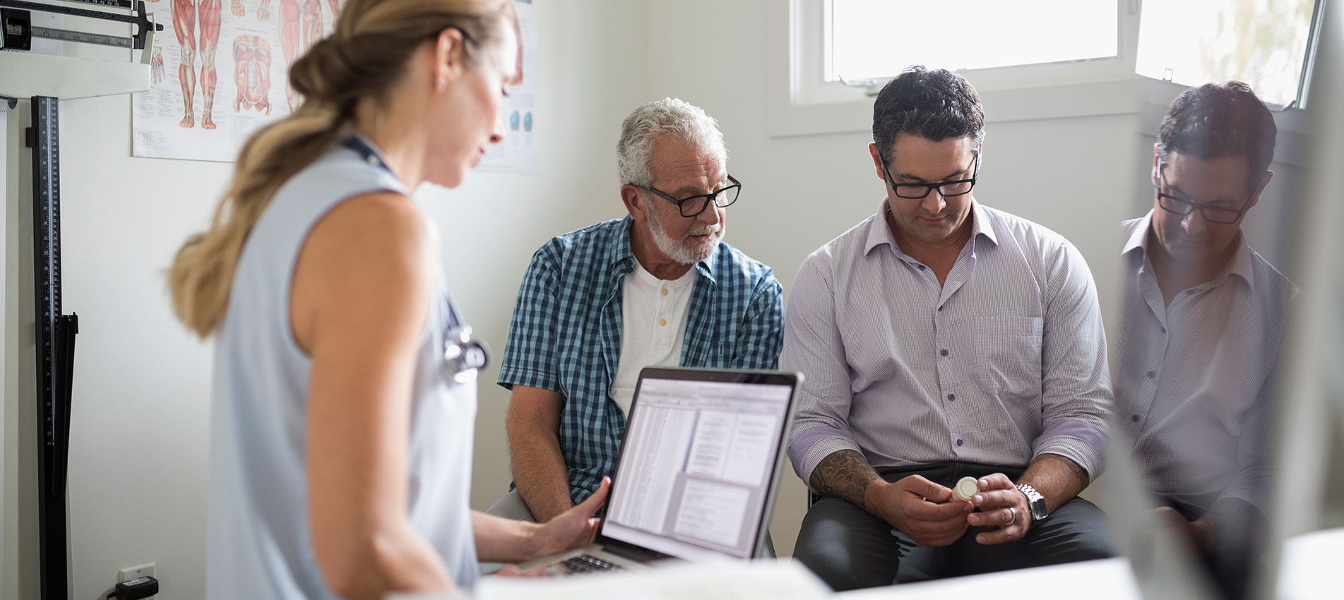 Female Doctor With Laptop Senior Male Patient And Son Prescription