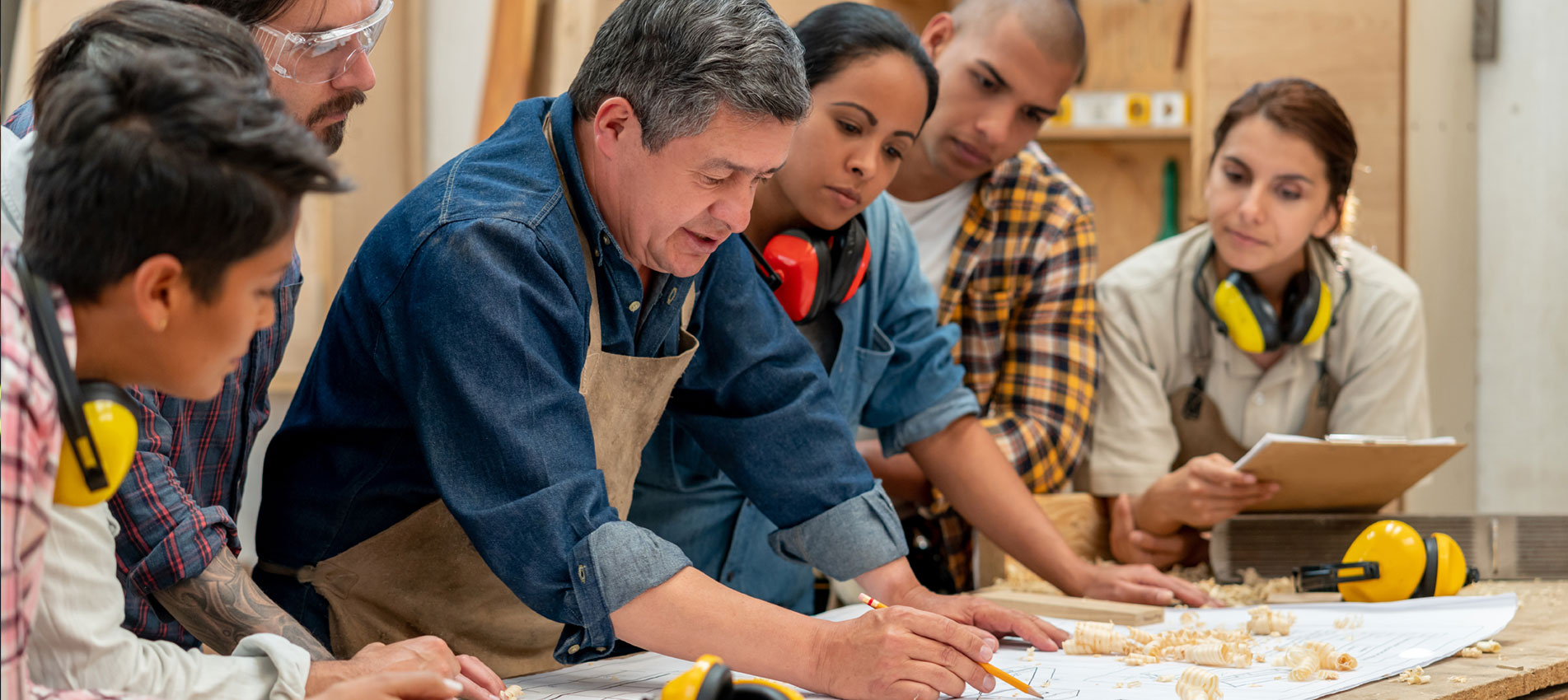Group Of Workers At A Furniture Factory Looking At A Blueprint