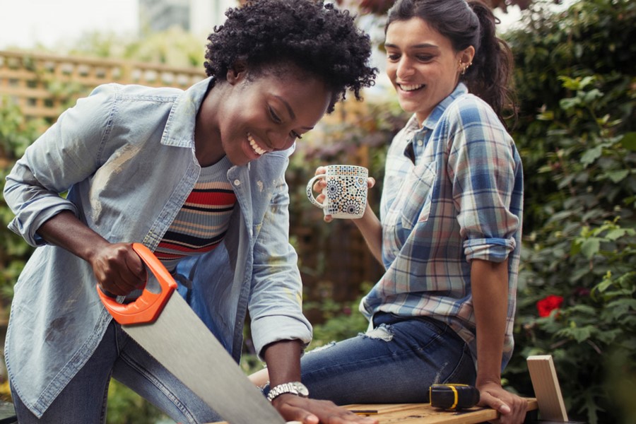 Women Drinking Coffee And Cutting Wood With Saw On Patio
