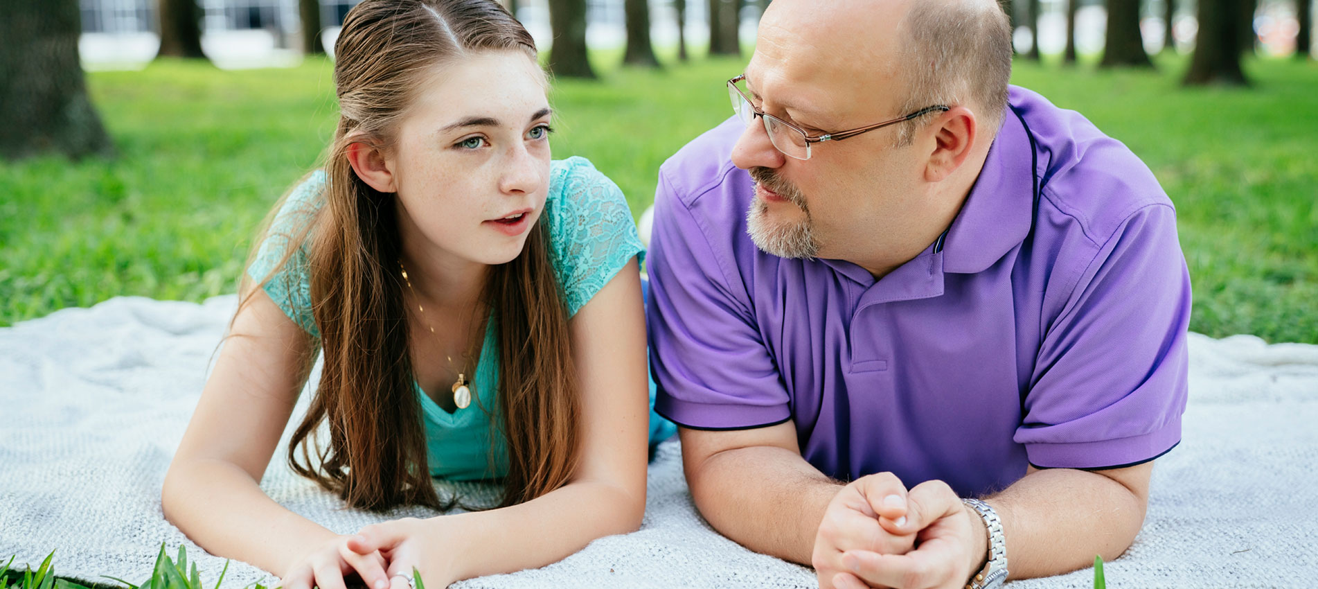 Serious Caucasian Father And Daughter Talking On Blanket In Park