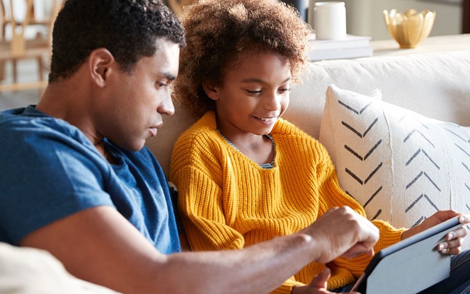 Daughter And Father Sitting On The Sofa Using A Tablet