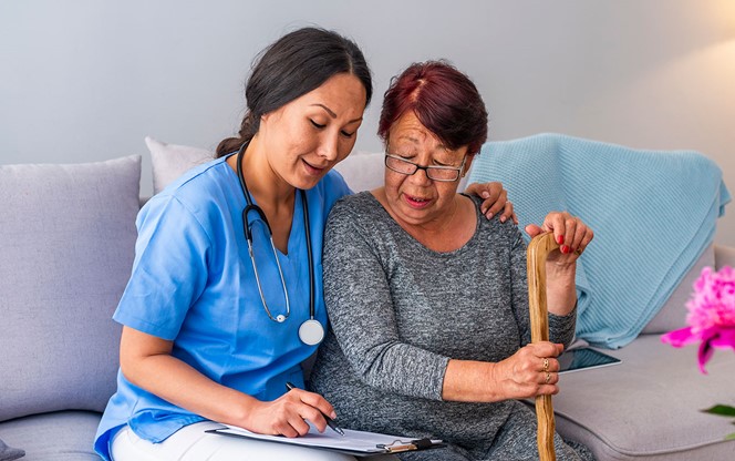 Smiling Senior Woman With Walking Stick And Helpful Caregiver Holding Her Hand