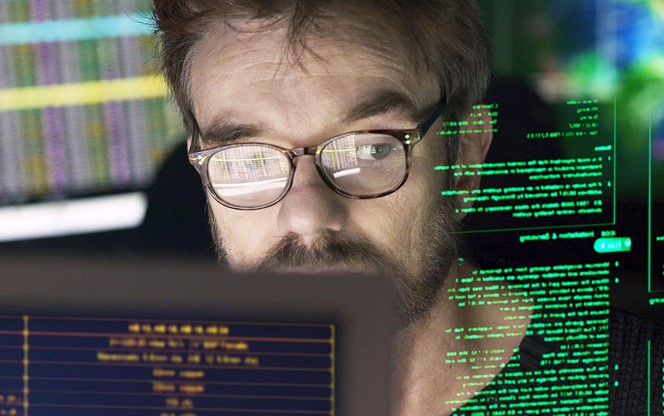 Stock close-up photo of a mature man surrounded by monitors & a holographic display which he is reading