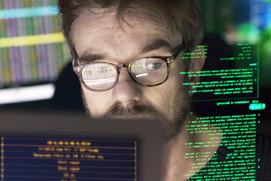Stock close-up photo of a mature man surrounded by monitors & a holographic display which he is reading