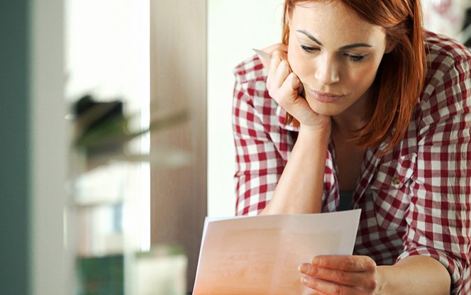 Closeup of attractive mid 30's housewife looking at monthly bills that seem to have skyrocketed