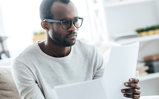 Young African man working with documents while sitting on the sofa at home