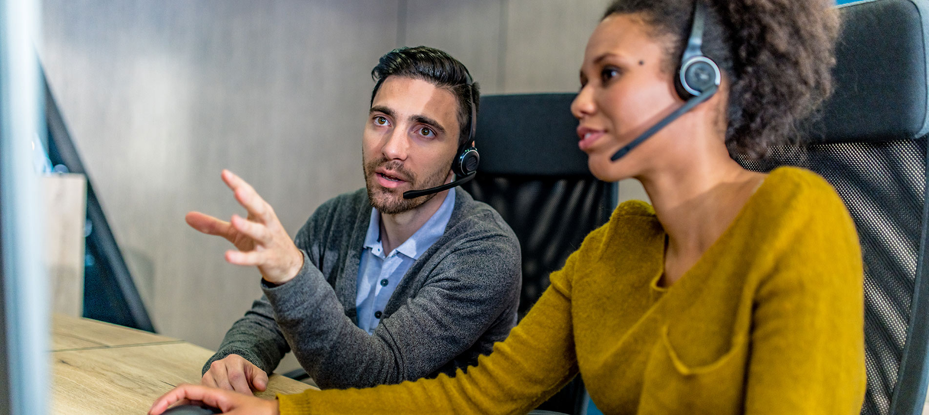 Man Working In A Call Centre Helping His Female Colleague While They Are Using A Computer