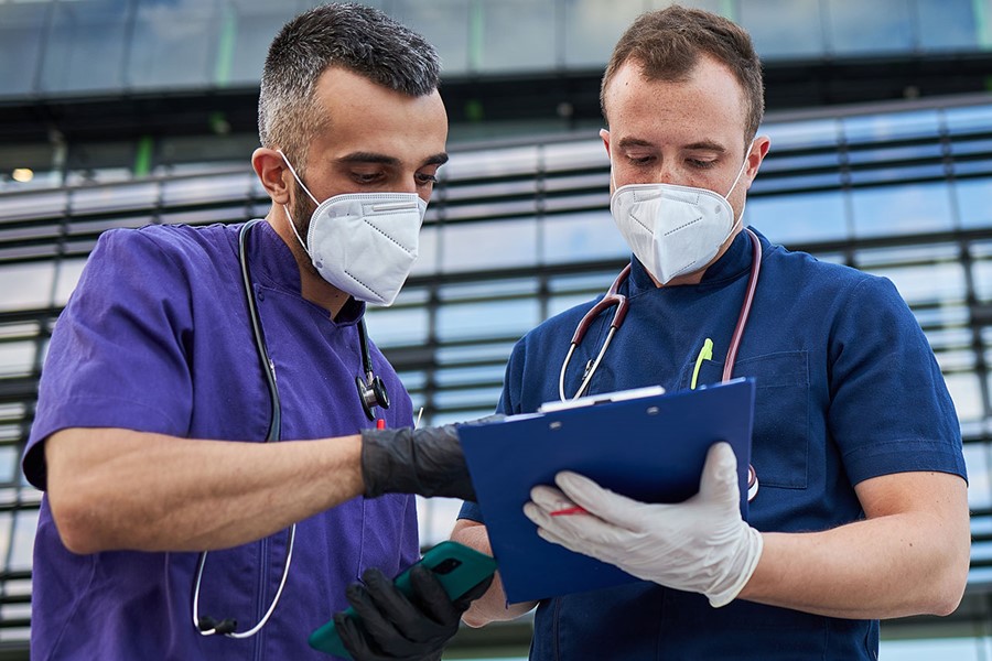 Medical Colleagues Working With A Note Pad And Statistics In Front Of A Hospital