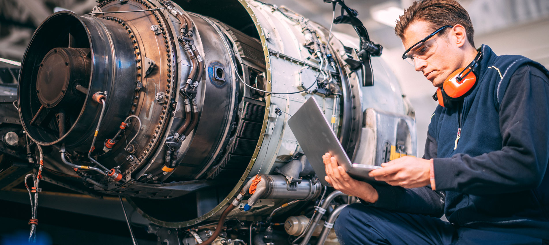 Aircraft Engineer In A Hangar Using A Laptop While Repairing And Maintaining An Airplane Jet Engine