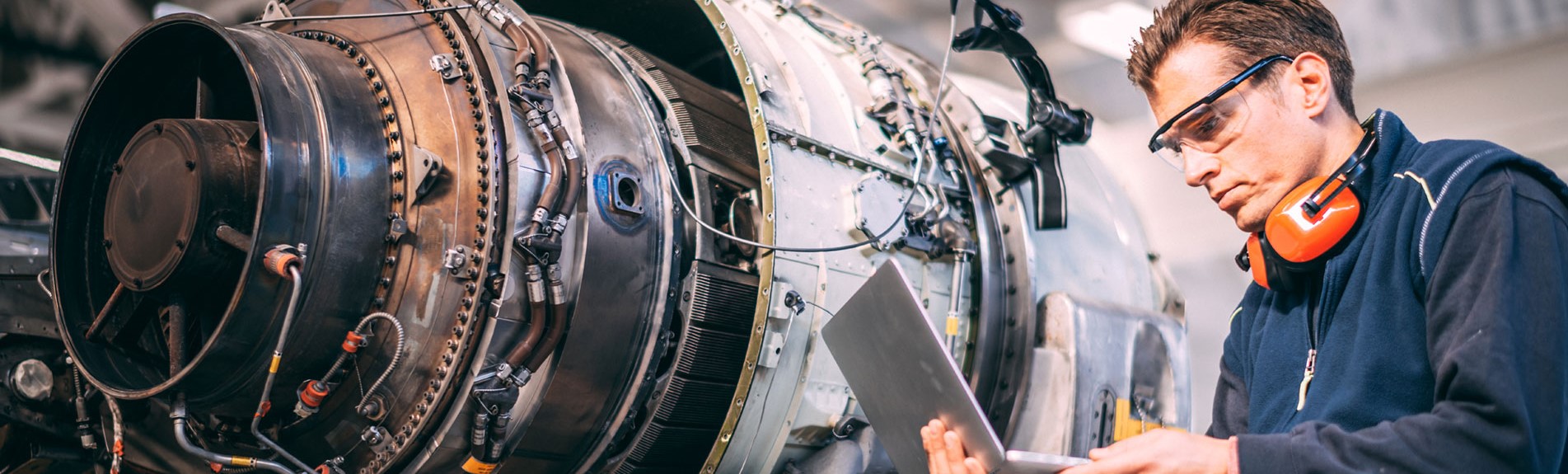 Aircraft Engineer In A Hangar Using A Laptop While Repairing And Maintaining An Airplane Jet Engine
