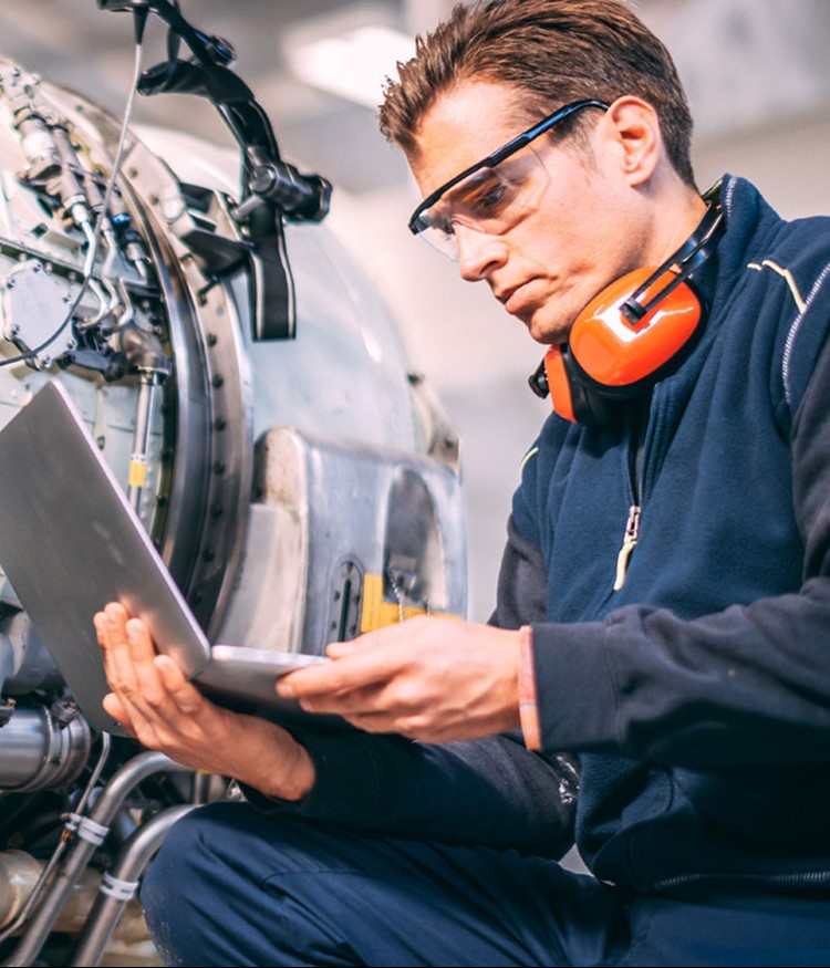 Aircraft Engineer In A Hangar Using A Laptop While Repairing And Maintaining An Airplane Jet Engine