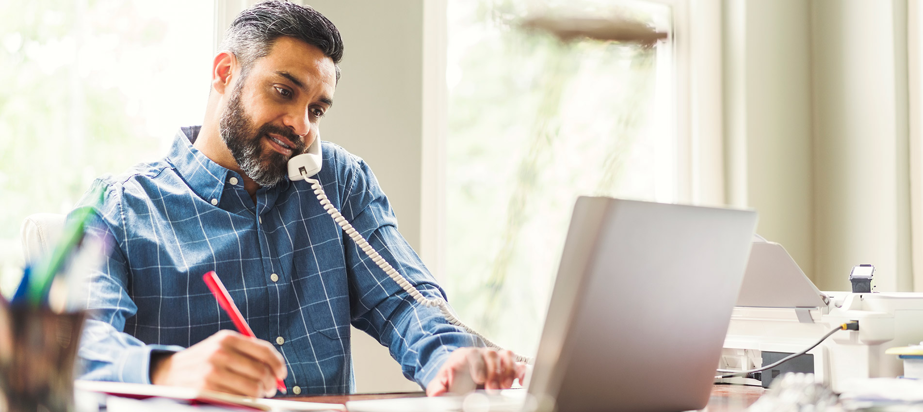 Mid Adult Businessman Using Phone And Laptop At Home Office