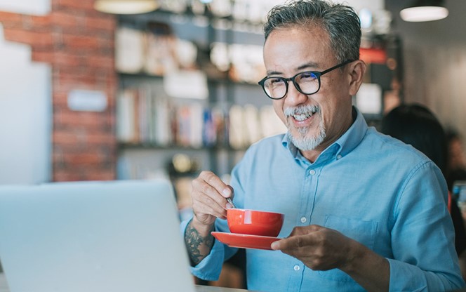 An Asian Chinese Senior Man Having Coffee In A Cafe Looking At His Laptop