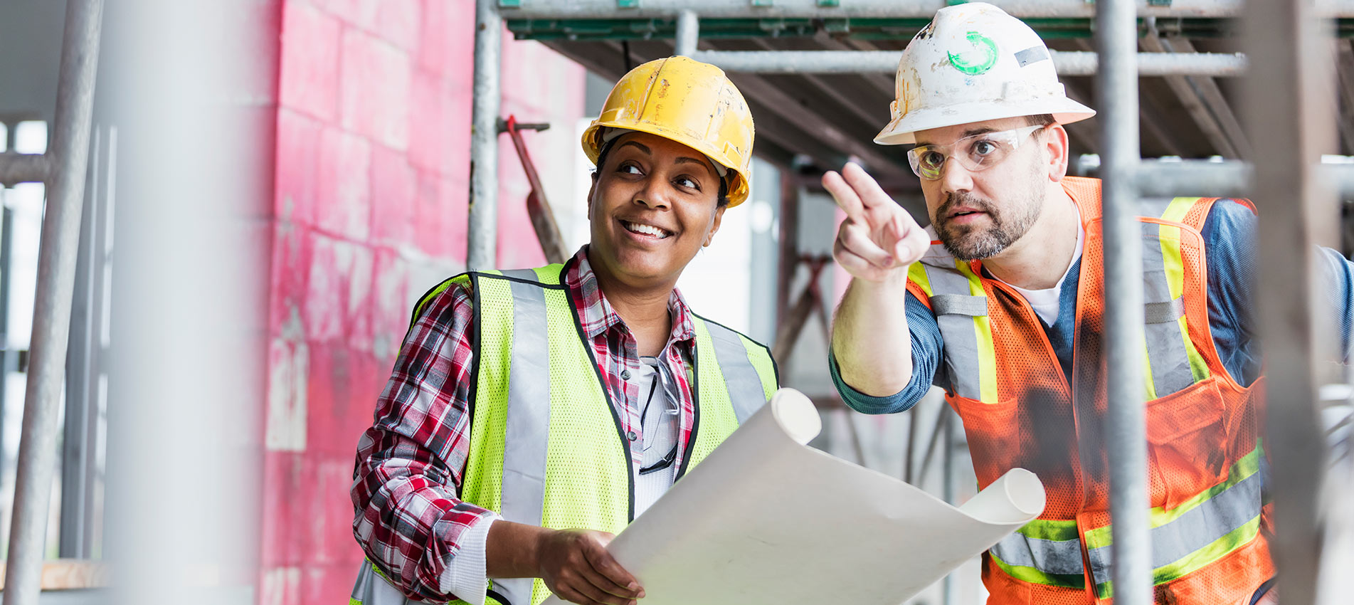 African American Female And Hispanic Male Construction Workers At A Construction Site Looking At A Plan