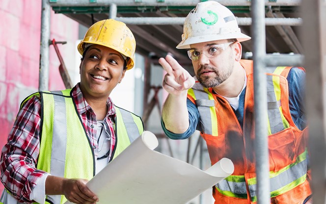 African American Female And Hispanic Male Construction Workers At A Construction Site Looking At A Plan