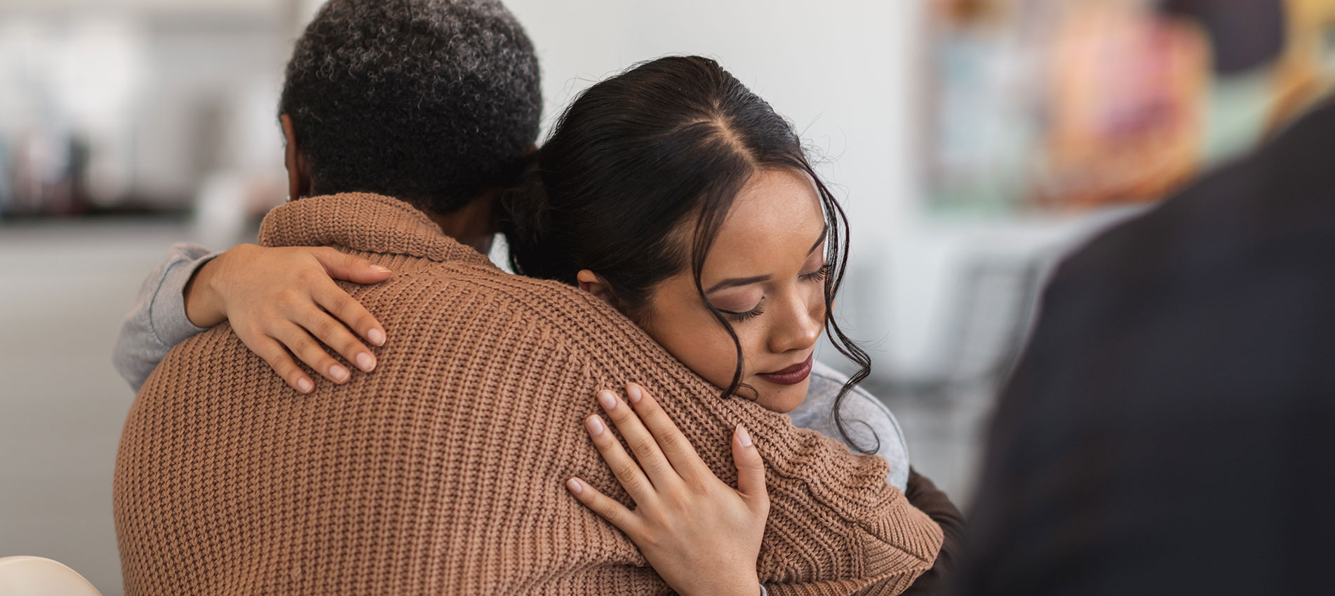 A Young Mixed Race Woman Hugs A Mature Adult Black Woman At A Group Therapy Session