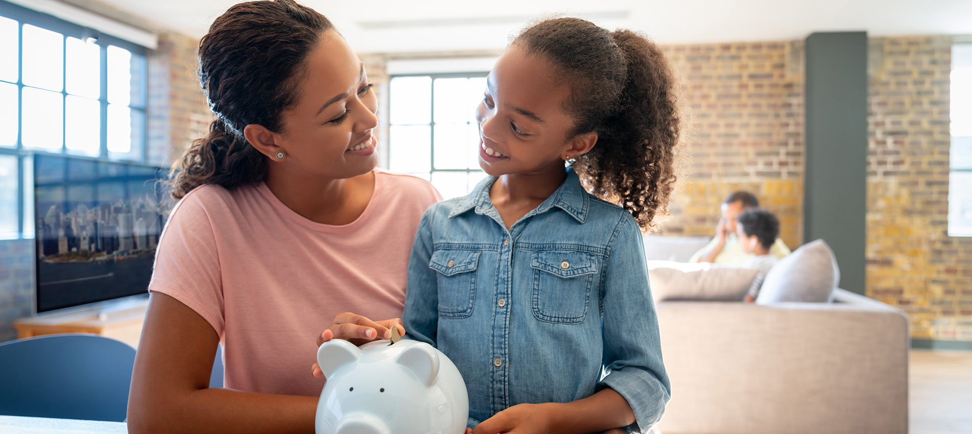 Mother And Daughter Saving Money In A Piggybank