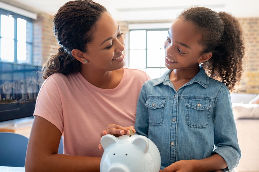 Mother And Daughter Saving Money In A Piggybank