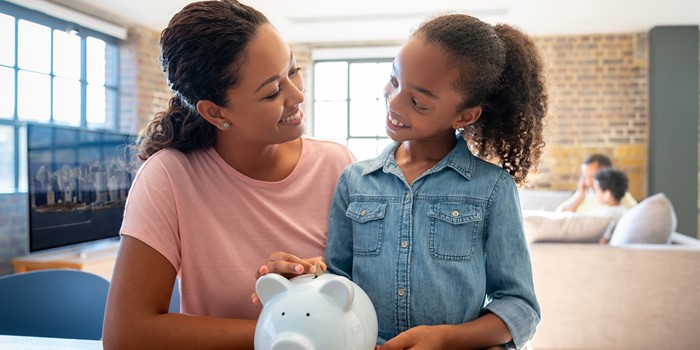Mother And Daughter Saving Money In A Piggybank