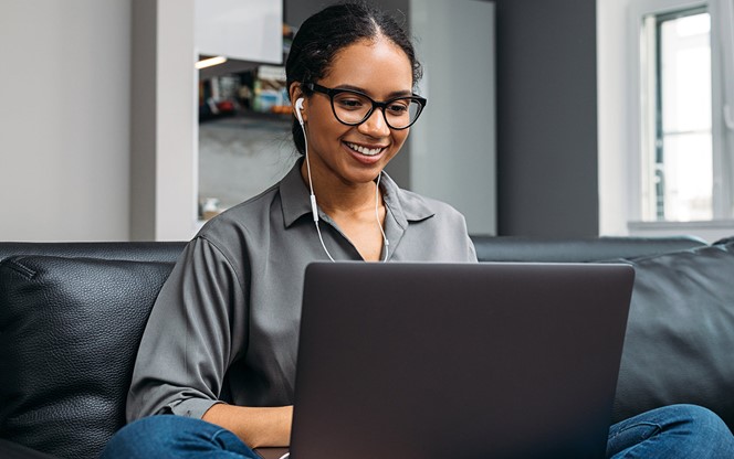 Young Woman Video Calling Using A Laptop Sitting On A Sofa Wearing Earphones