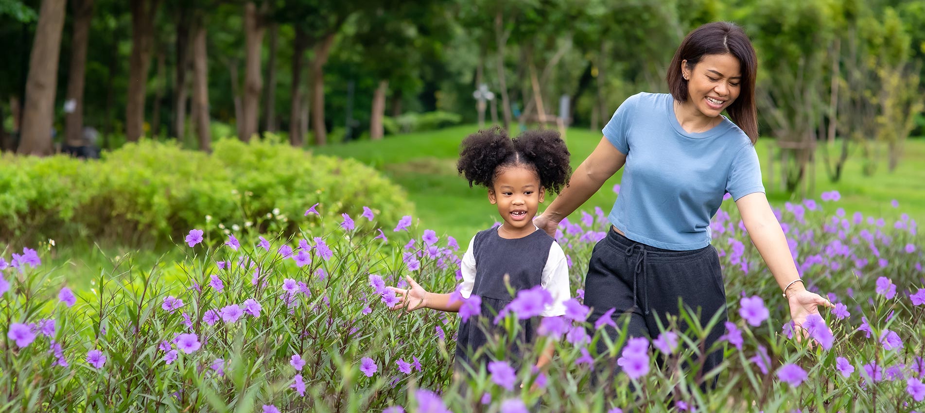 Happy Mixed Race Mother With Little Daughter Holding Hands And Walking Together In The Garden