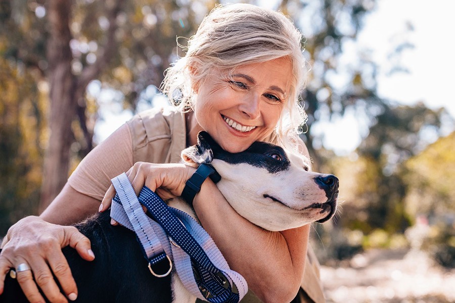Affectionate Mature Woman Embracing Pet Dog In Nature