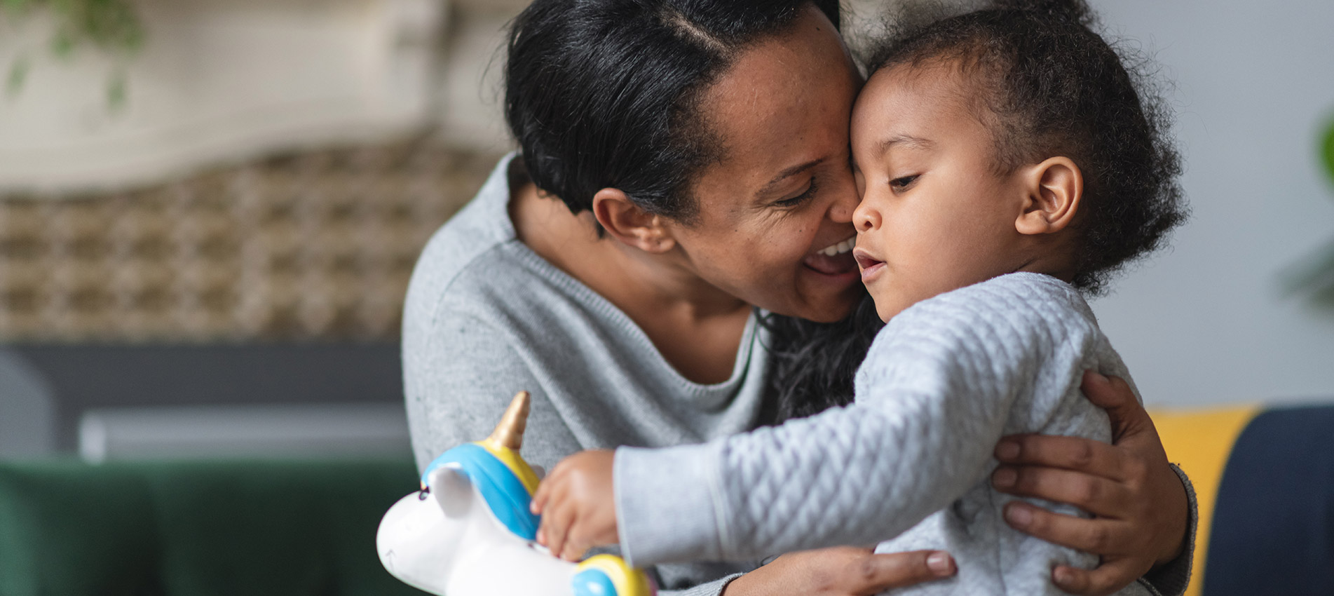 African American Mother Is Hugging Her Baby Son Proudly While He Is Putting Money Away In A Piggy Bank