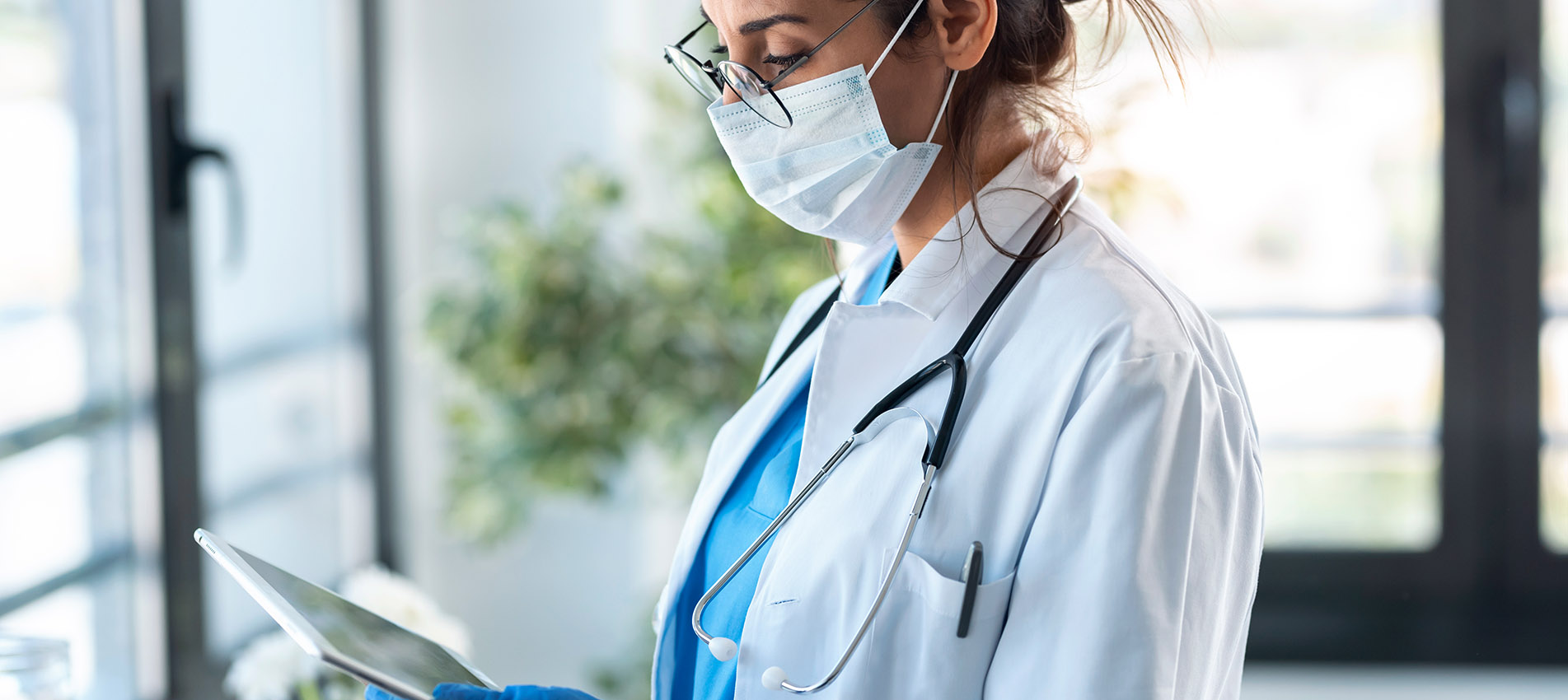 Female Doctor Wearing Mask Looking At Tablet