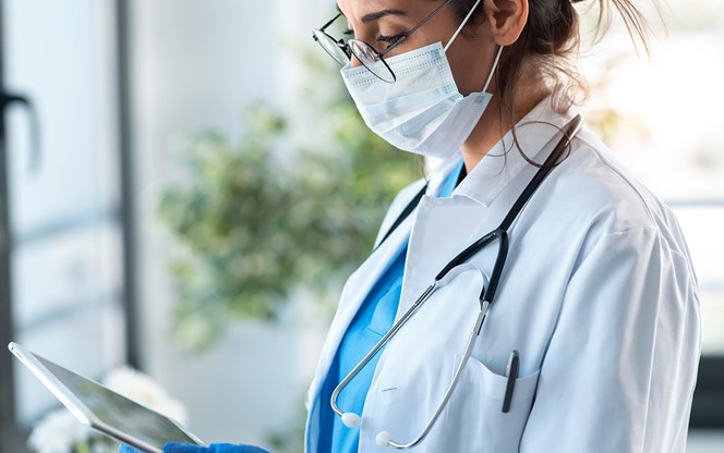 Female Doctor Wearing Mask Looking At Tablet