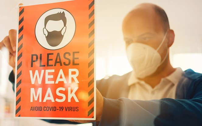 Man With Face Mask Putting Please Wear Mask Sign At Office