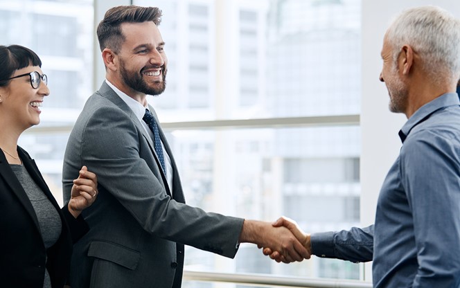 Two Businessmen Shaking Hands While Their Colleagues Look On