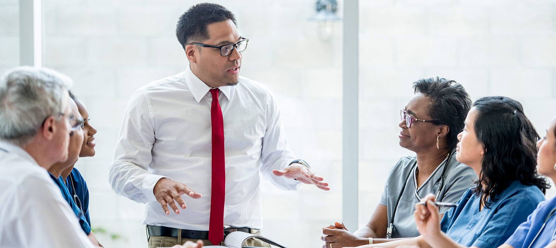An Ethnic Male Doctor Is Giving A Presentation To The Team