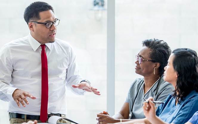 An Ethnic Male Doctor Is Giving A Presentation To The Team